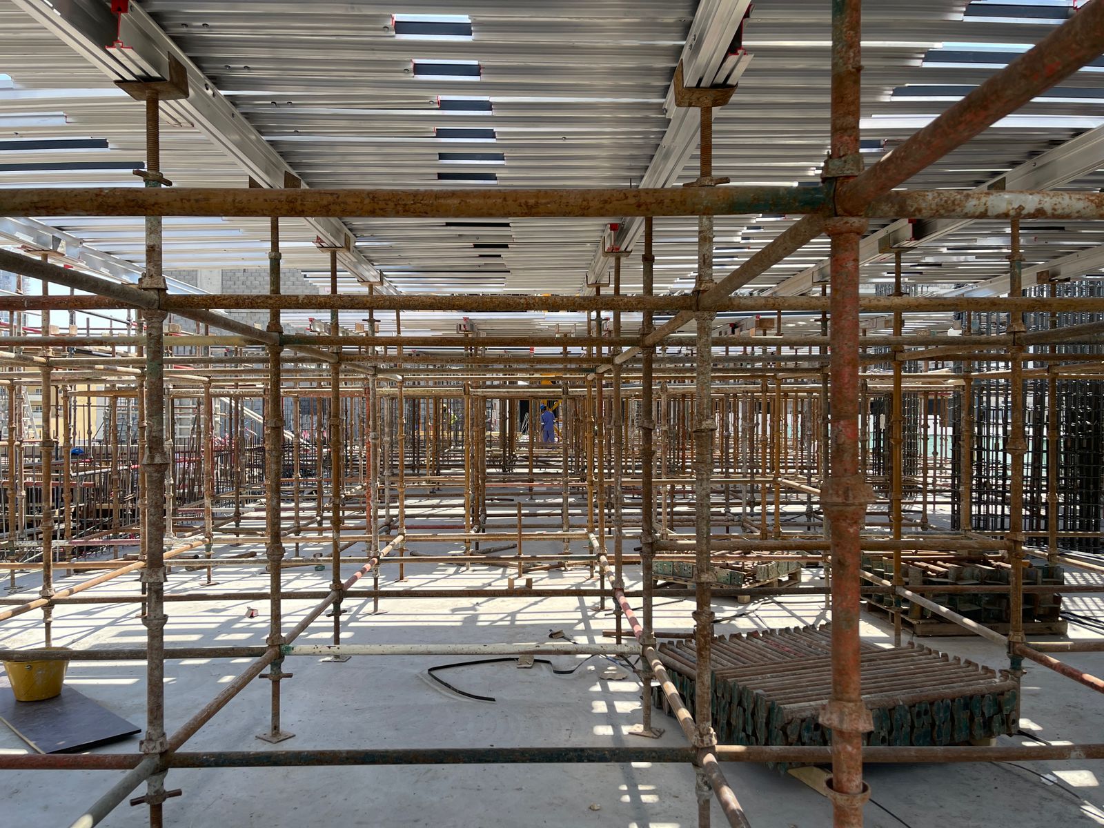 Pearl House By Imtiaz Scaffolding structures fill an under-construction area, with beams overhead and concrete materials nearby.